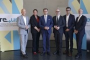 Sechs Personen, fünf Männer und eine Frau, stehen nebeneinander für ein Gruppenfoto vor einer Wand mit blau-gelben Grafikelementen und einem Banner zur Initiative „re-use“. Sie tragen Businesskleidung und blicken in die Kamera.